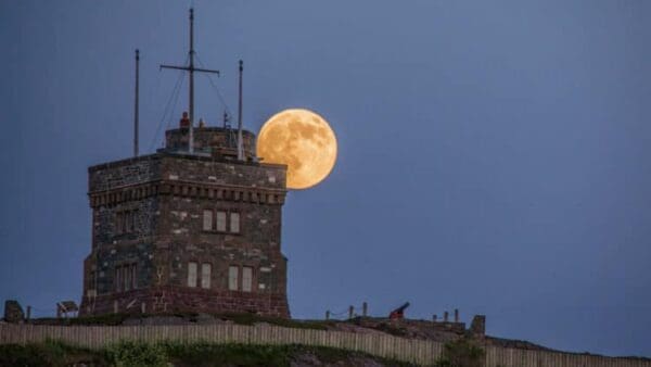 A full moon rises over the top of a tower.