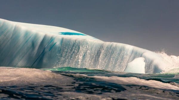 A wave is shown in the ocean with water behind it.