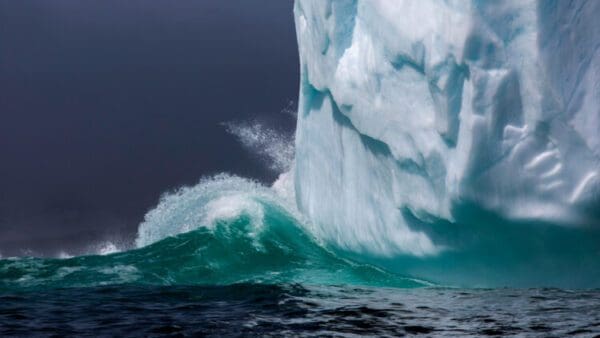 A large wave is crashing against the side of an iceberg.
