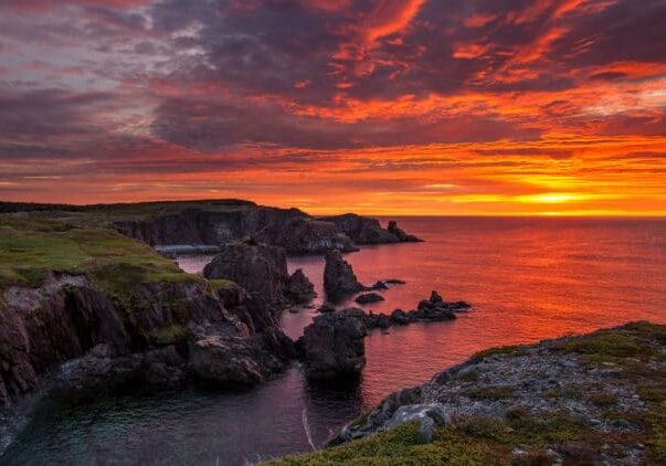 A sunset over the ocean with rocks in the foreground.